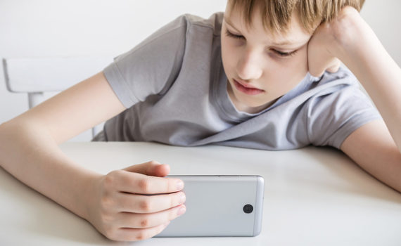 Child sitting at a table looking at a phone.
