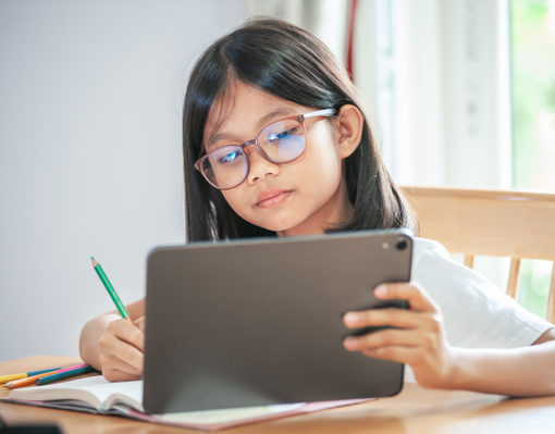Child writing in a notebook while looking at a tablet