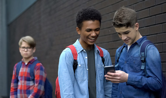Two teens standing outside looking a phone screen together.