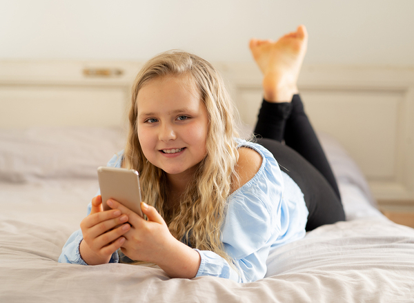 Teen female lying on a bed looking at her cell phone.