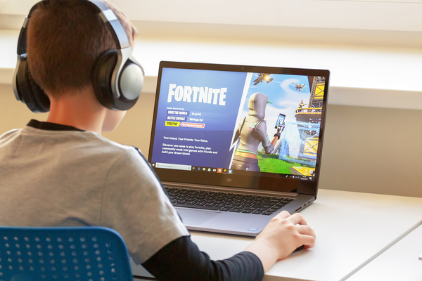Young teen playing Fortnite on a laptop.