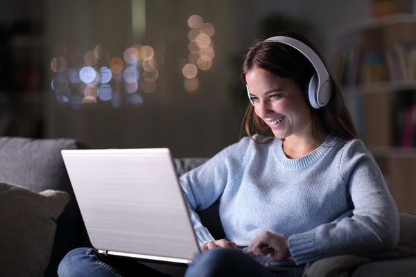 Woman wearing headphones looking at a laptop screen.