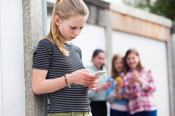 Young teen leaning against a wall looking at her phone.