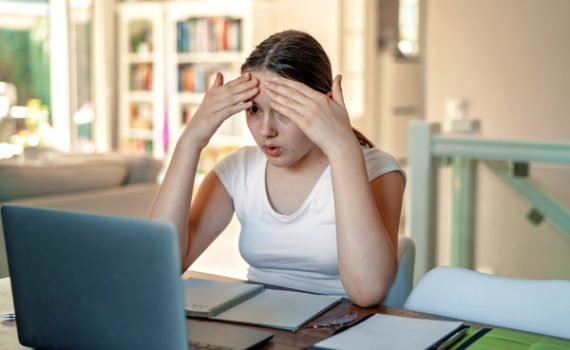 Teen with her hands on her forehead looking at a computer screen.