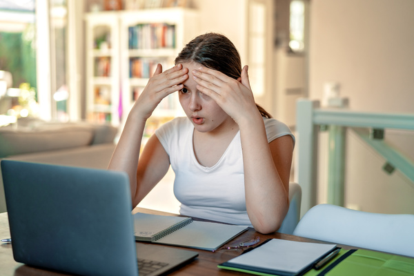 Teen with her hands on her forehead looking at a computer screen.