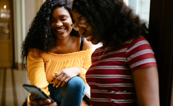 Two teens smiling while looking at a phone screen.