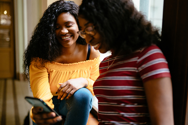Two teens smiling while looking at a phone screen.